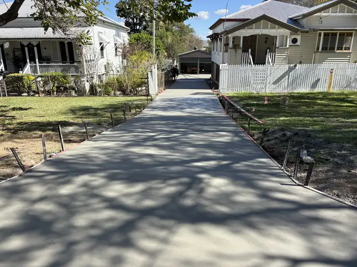 A long new concrete driveway running between two Queenslander homes to a garage at the back
