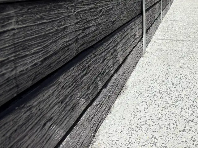 A light exposed aggregate house surround beside a charcoal timber-look concrete sleeper wall in Ripley